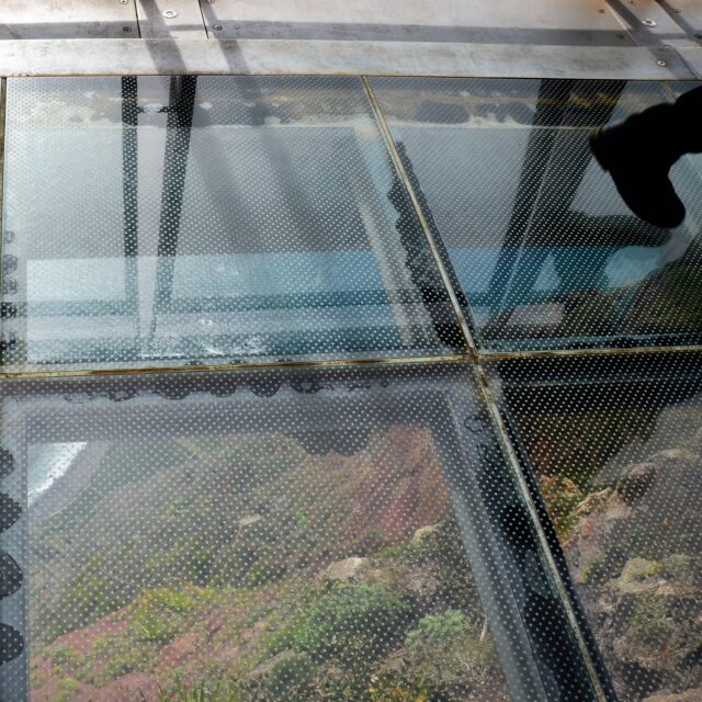 A glass-floored viewpoint overlooking a steep drop with the ocean below.