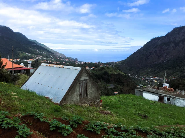Coastal scenery from the levada path with vegetable gardens and traditional rooftops.