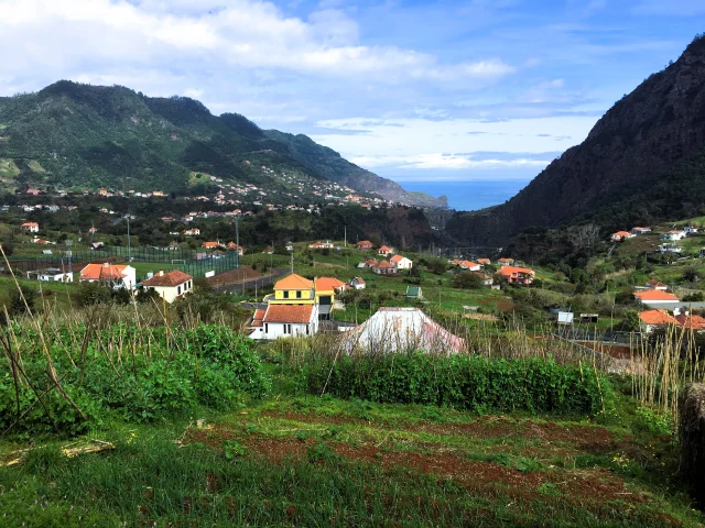 Levada walk with rural houses and green hills under a clear blue sky in Madeira’s north coast.
